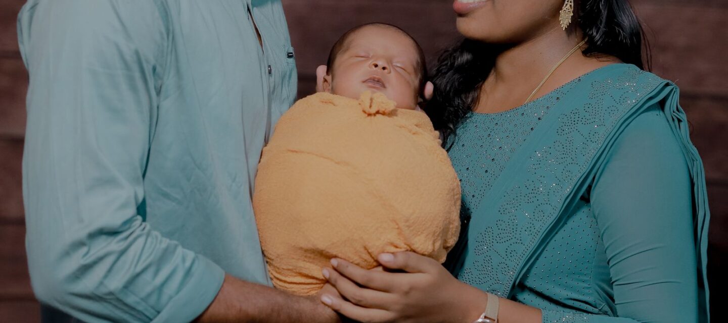Happy Indian couple with newborn baby in a warm studio portrait — Photo: Dream_maKkerzz / Pexels (free to use)