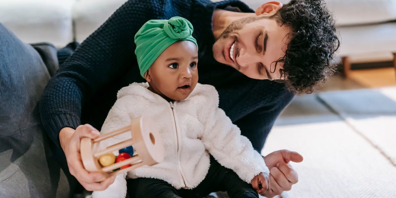 Indian father in a modern living room smiling while playing with his baby girl on a light rug