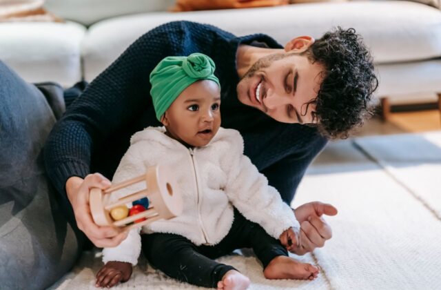 Indian father in a modern living room smiling while playing with his baby girl on a light rug