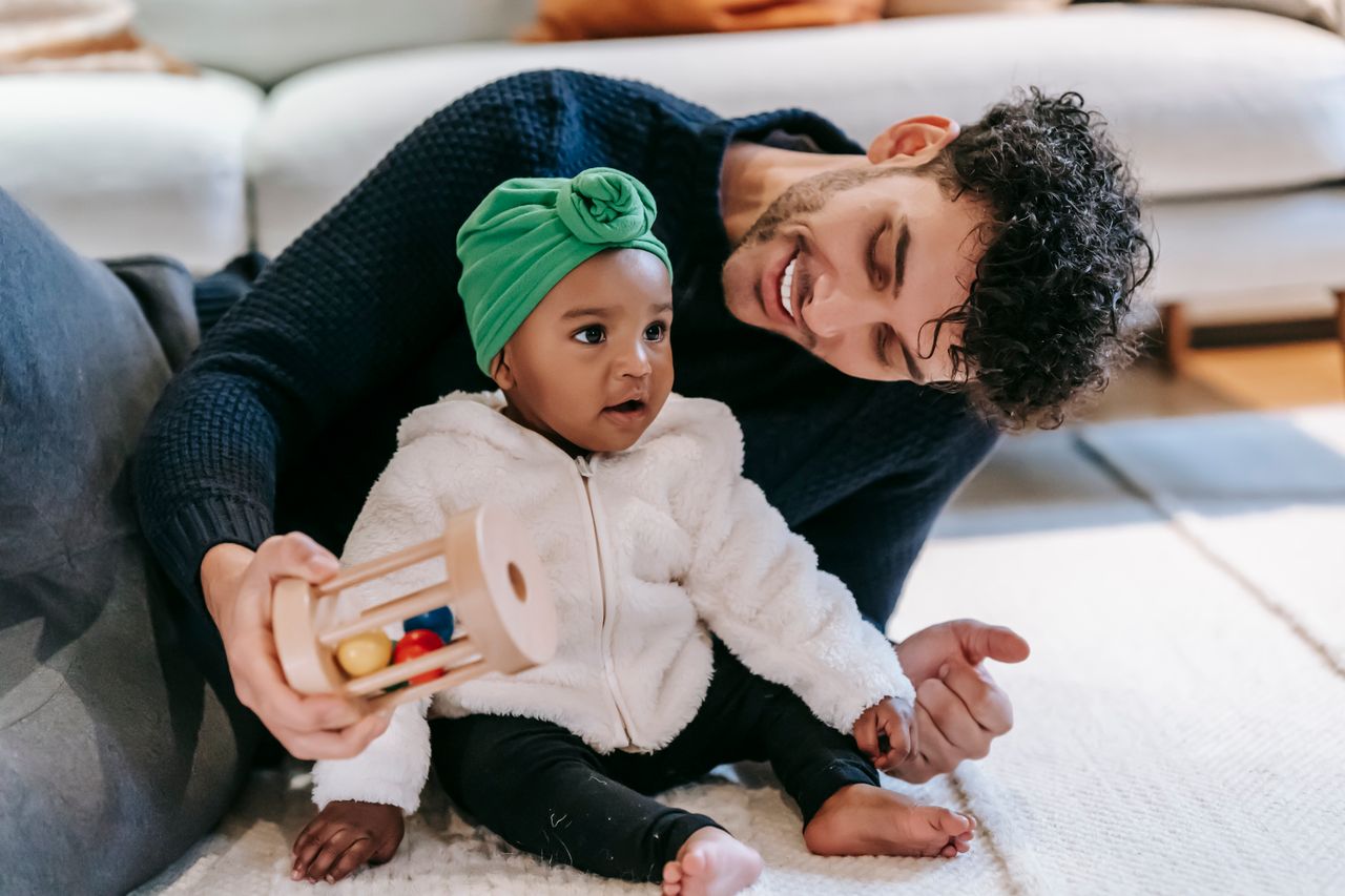Indian father in a modern living room smiling while playing with his baby girl on a light rug