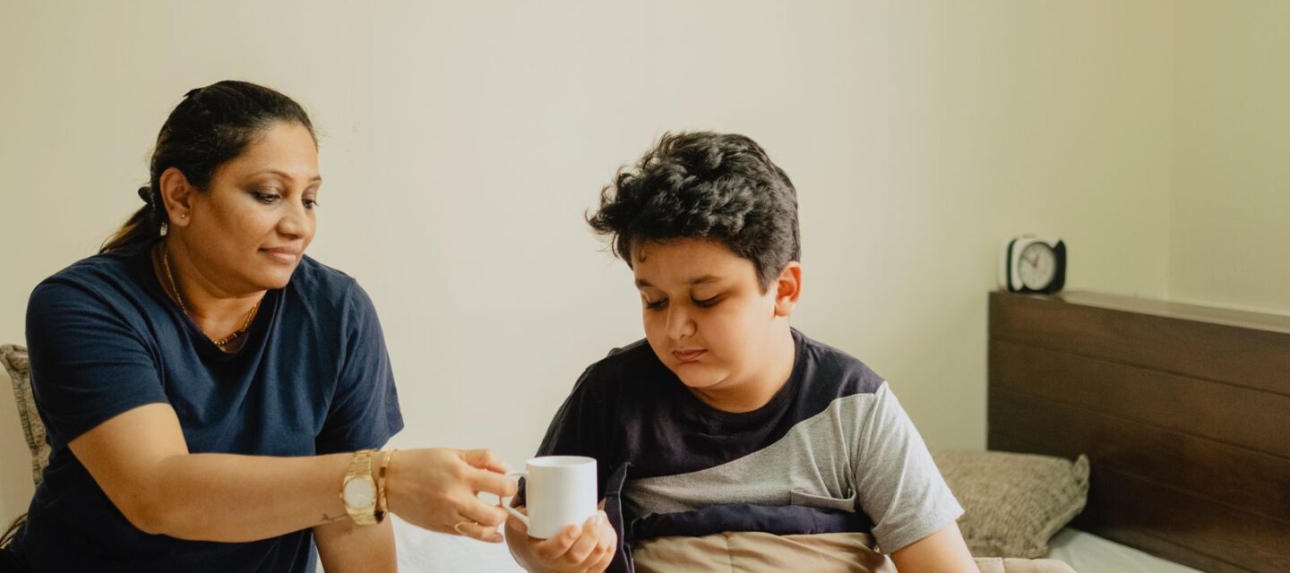 Indian mother caring for her mildly unwell son resting in bed at home, photo by Vivaan Rupani on Pexels