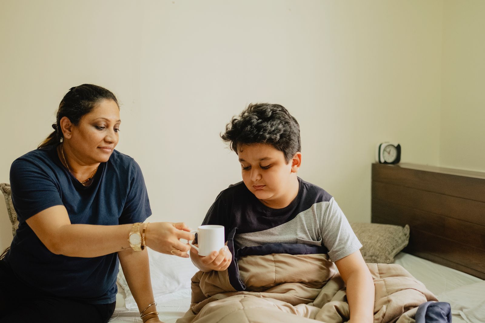 Indian mother caring for her mildly unwell son resting in bed at home, photo by Vivaan Rupani on Pexels
