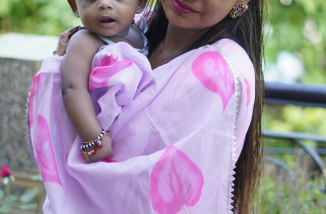 Well-dressed Indian mother holding her infant outdoors in a green garden setting