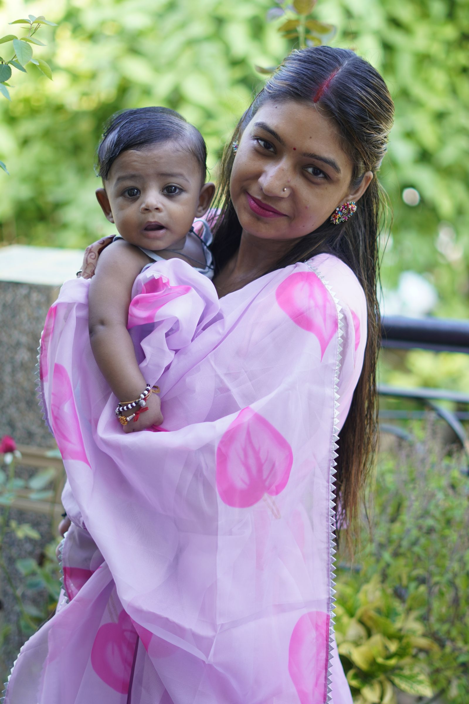 Well-dressed Indian mother holding her infant outdoors in a green garden setting