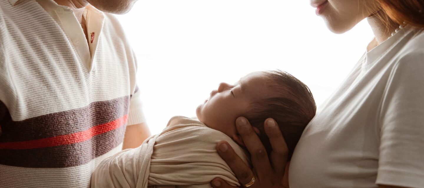 Well-to-do Asian parents cradling their swaddled newborn baby together