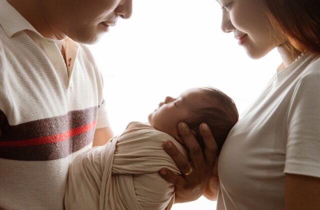 Well-to-do Asian parents cradling their swaddled newborn baby together