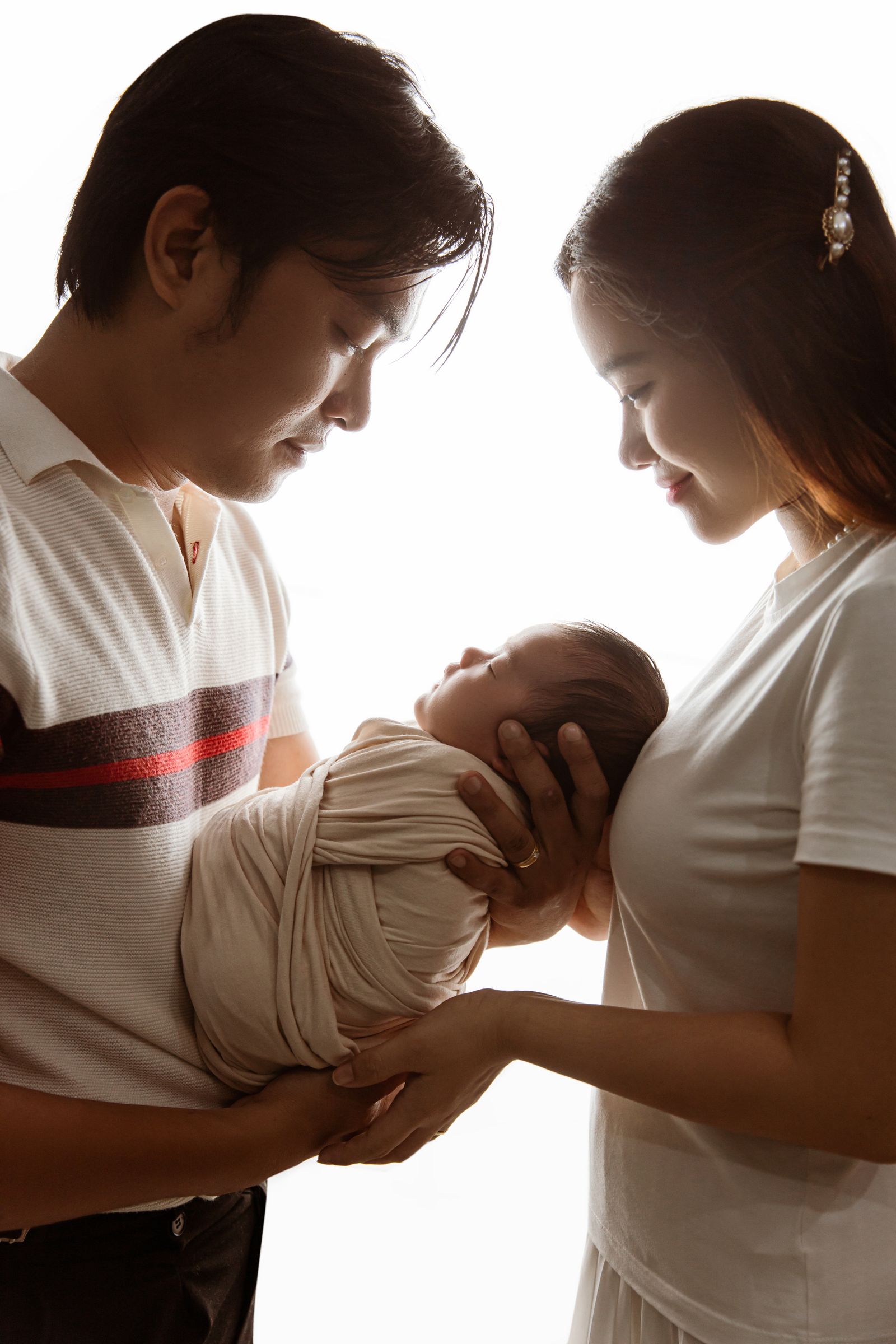 Well-to-do Asian parents cradling their swaddled newborn baby together