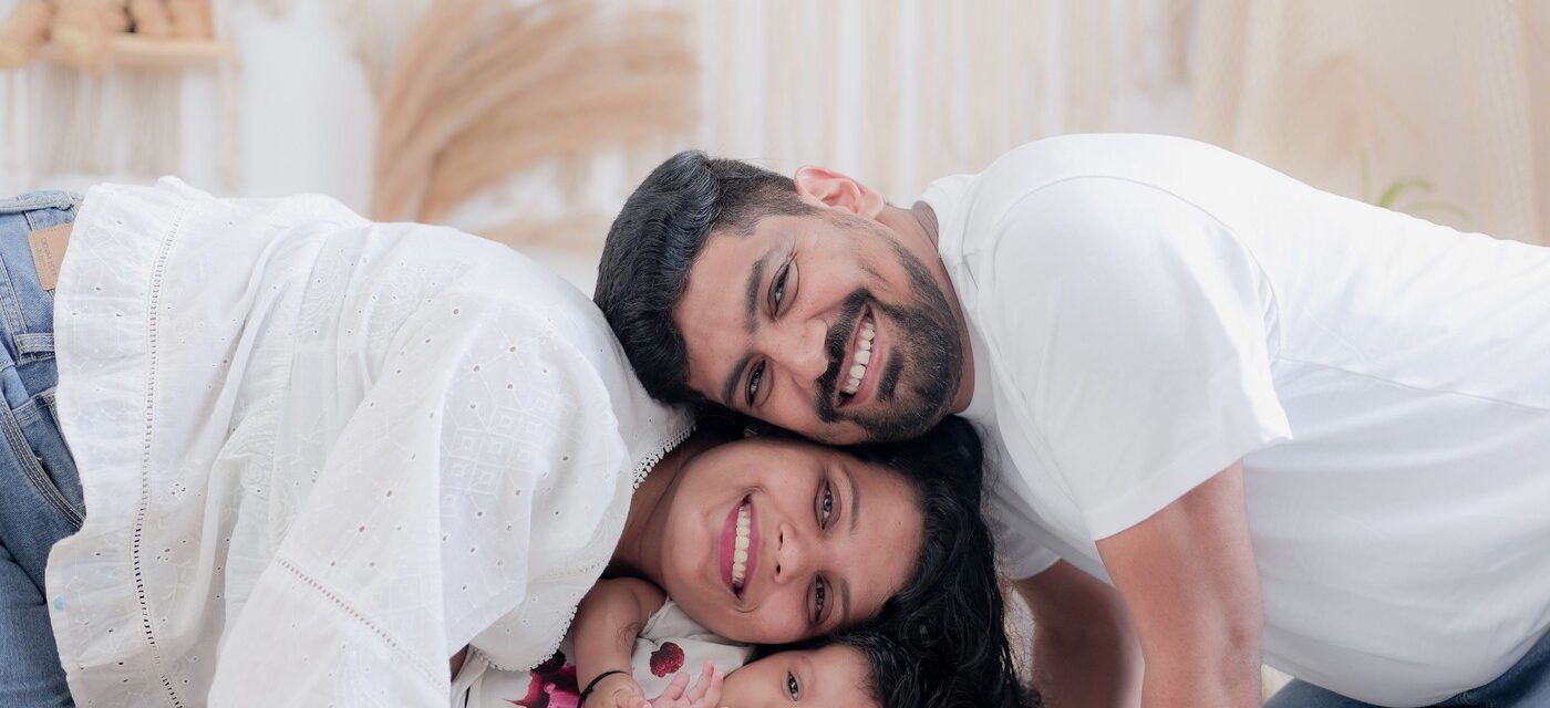 Smiling Indian mother, father and baby daughter cuddling together on a bed in a bright, modern home