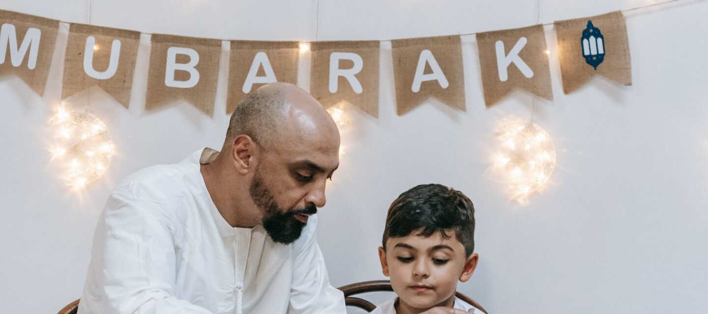 Well-dressed South Asian father and young son sharing a healthy home meal with rice and salad at the dining table