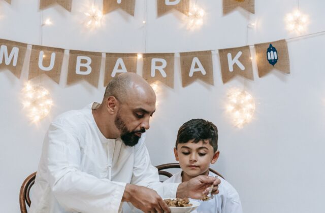 Well-dressed South Asian father and young son sharing a healthy home meal with rice and salad at the dining table
