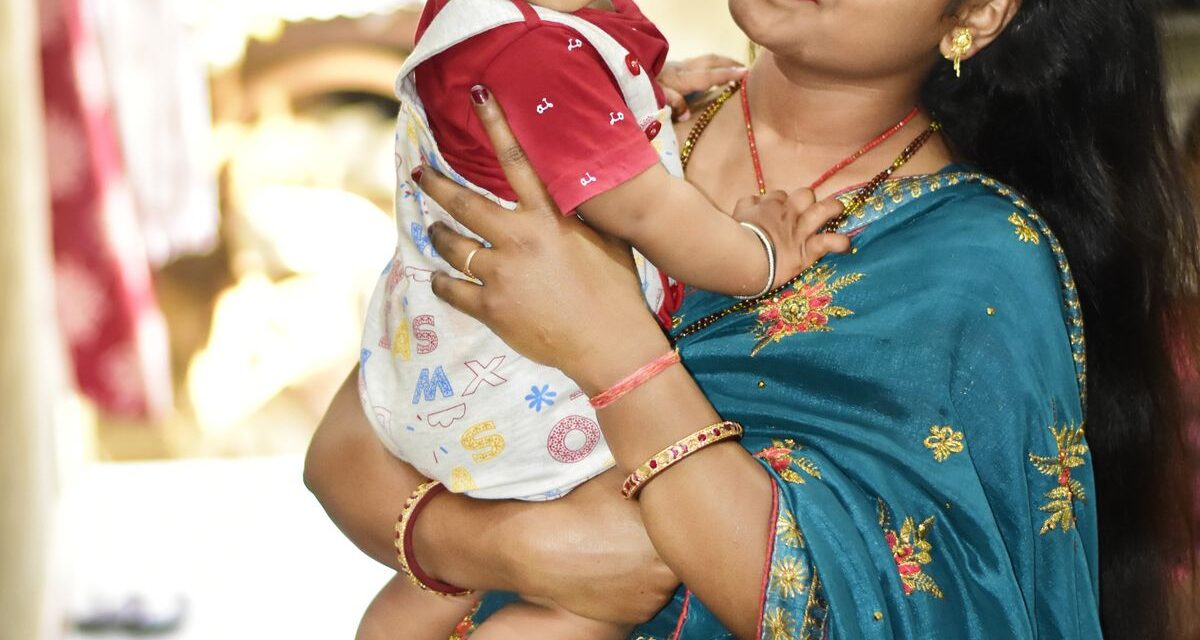 Well-dressed Indian mother in a saree gently holding her toddler indoors in a bright, comfortable home