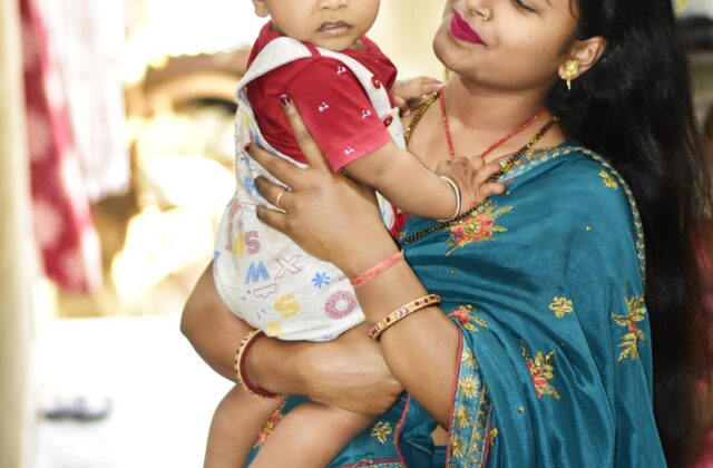 Well-dressed Indian mother in a saree gently holding her toddler indoors in a bright, comfortable home