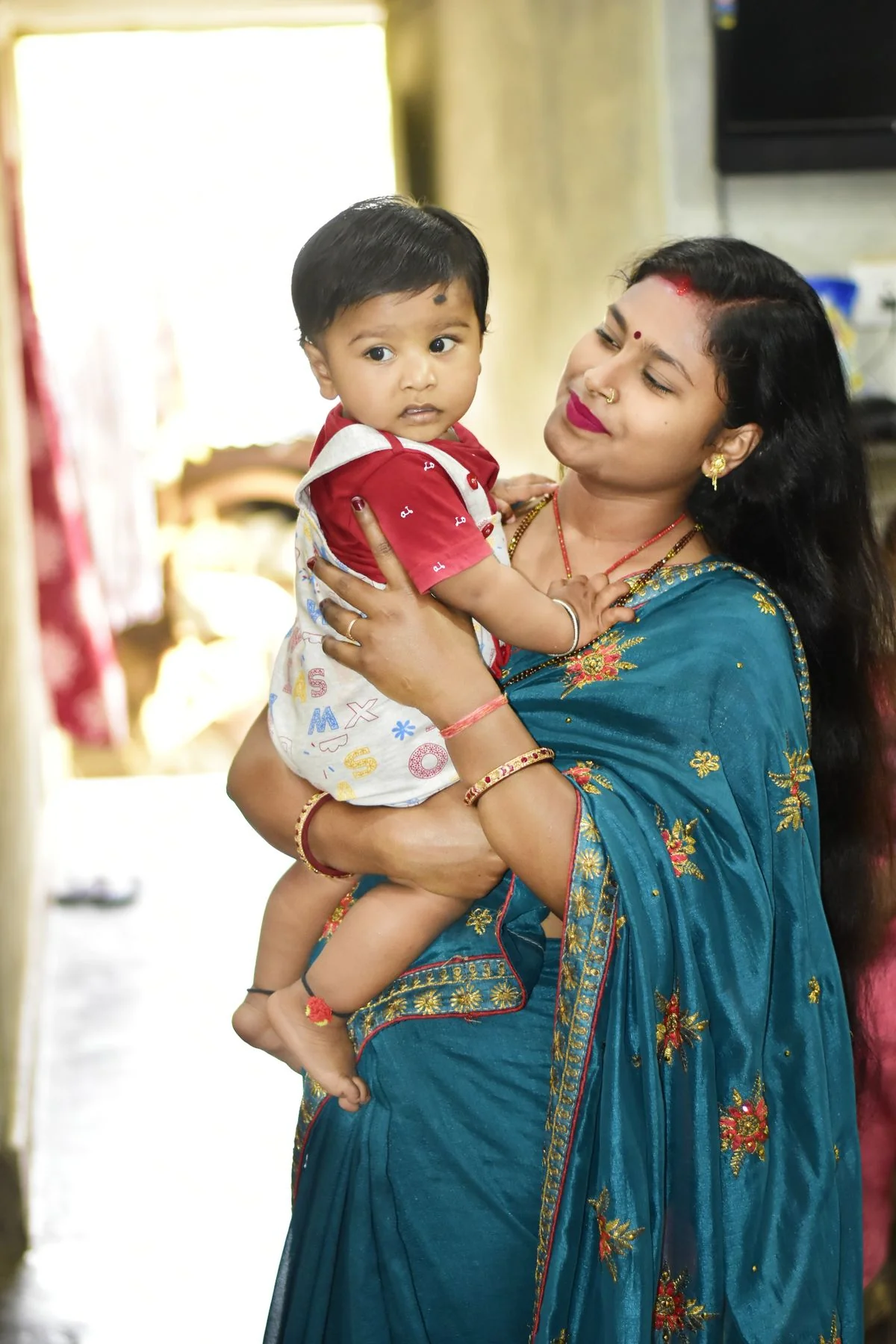 Well-dressed Indian mother in a saree gently holding her toddler indoors in a bright, comfortable home