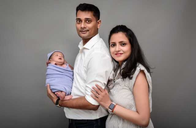 Smiling Indian parents holding their sleeping newborn baby, illustrating safe sleep for babies and SIDS prevention (photo: BabyBum Photography / Pexels)
