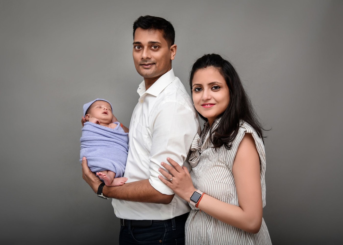 Smiling Indian parents holding their sleeping newborn baby, illustrating safe sleep for babies and SIDS prevention (photo: BabyBum Photography / Pexels)